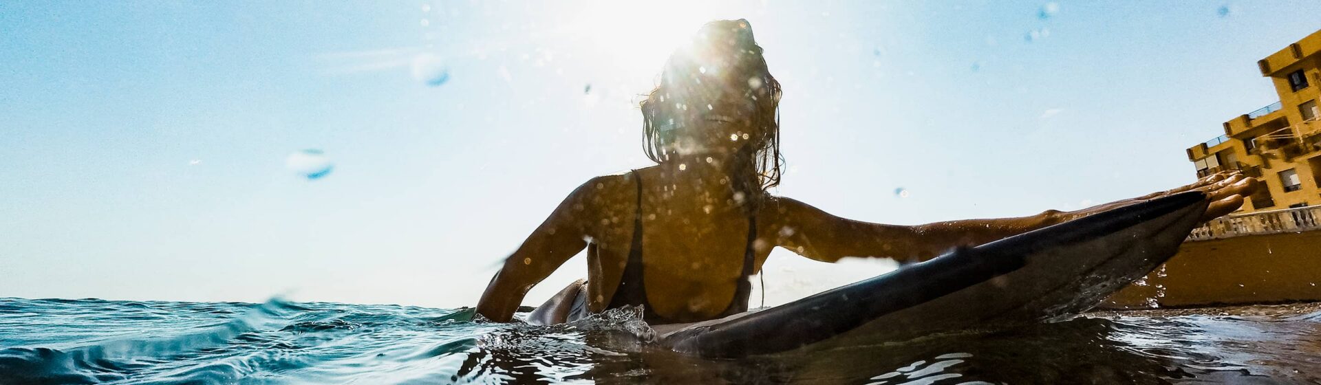 Jenny, featured in a HUB24 case study, smiling brightly as she paddles a surfboard in the ocean on a sunny day.